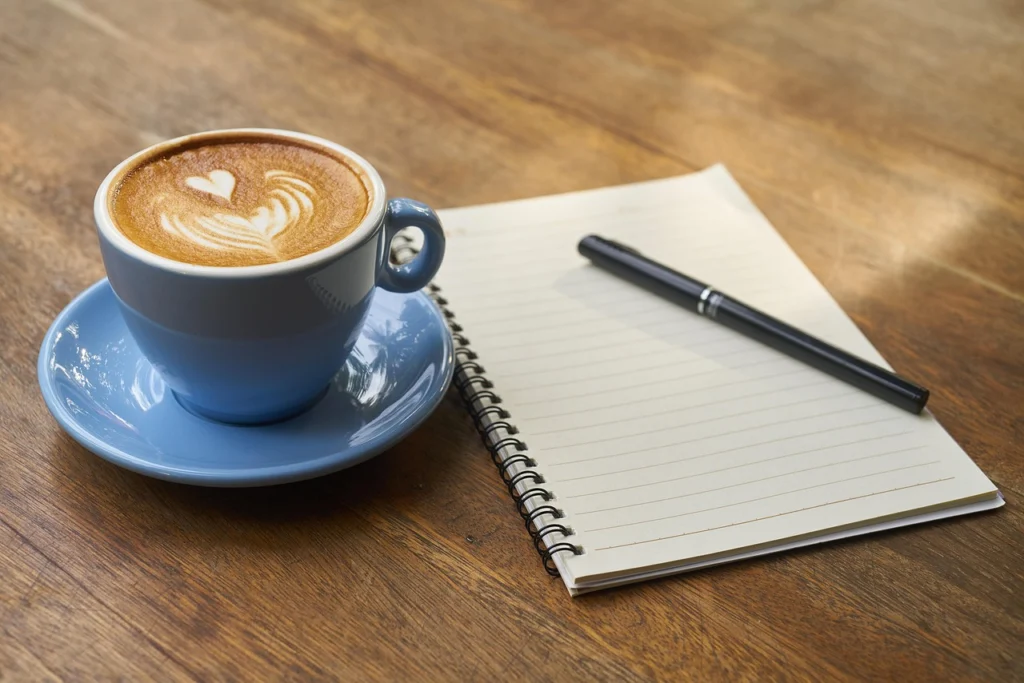 Notebook with pen and coffee next to a laptop, symbolizing the inventory step of a SERP features audit