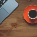 person working on laptop and drinking coffee at desk